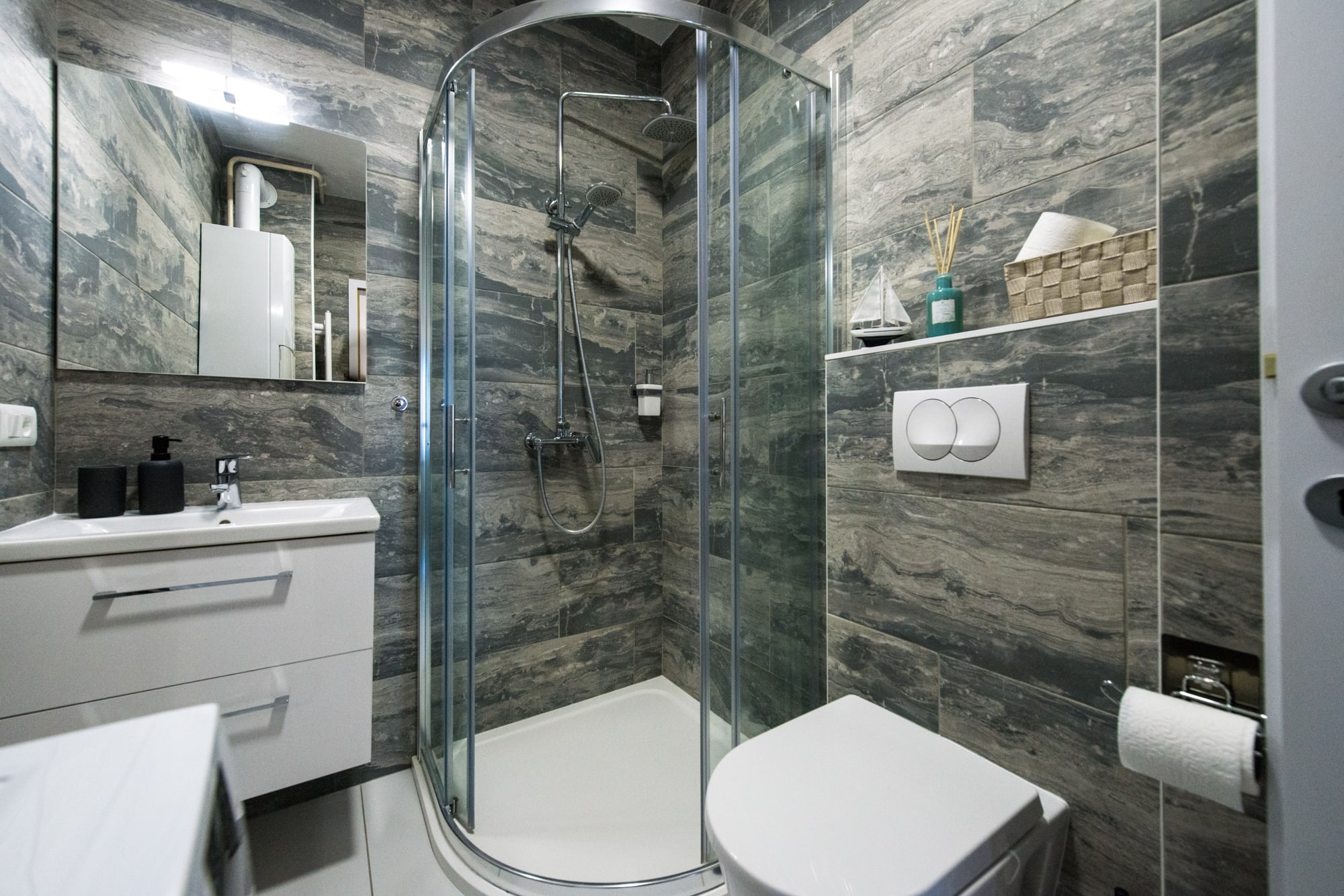Modern grey-tiled bathroom with glass shower, vanity and toilet
